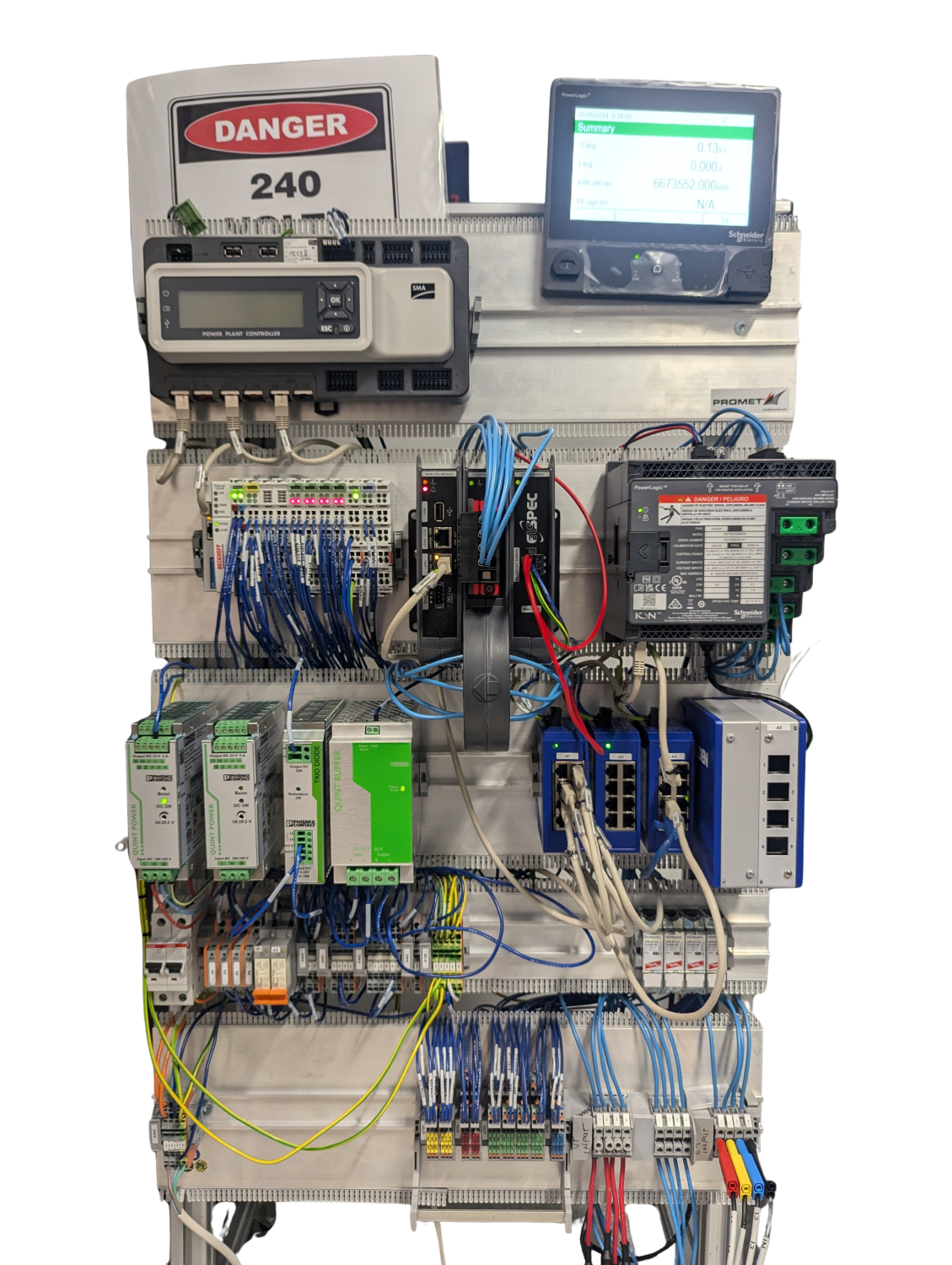 Industrial electrical control panel featuring multiple power modules, circuit breakers, programmable logic controllers (PLCs), Ethernet switches, and wiring, labeled with a "DANGER 240" warning sign and digital monitoring display.